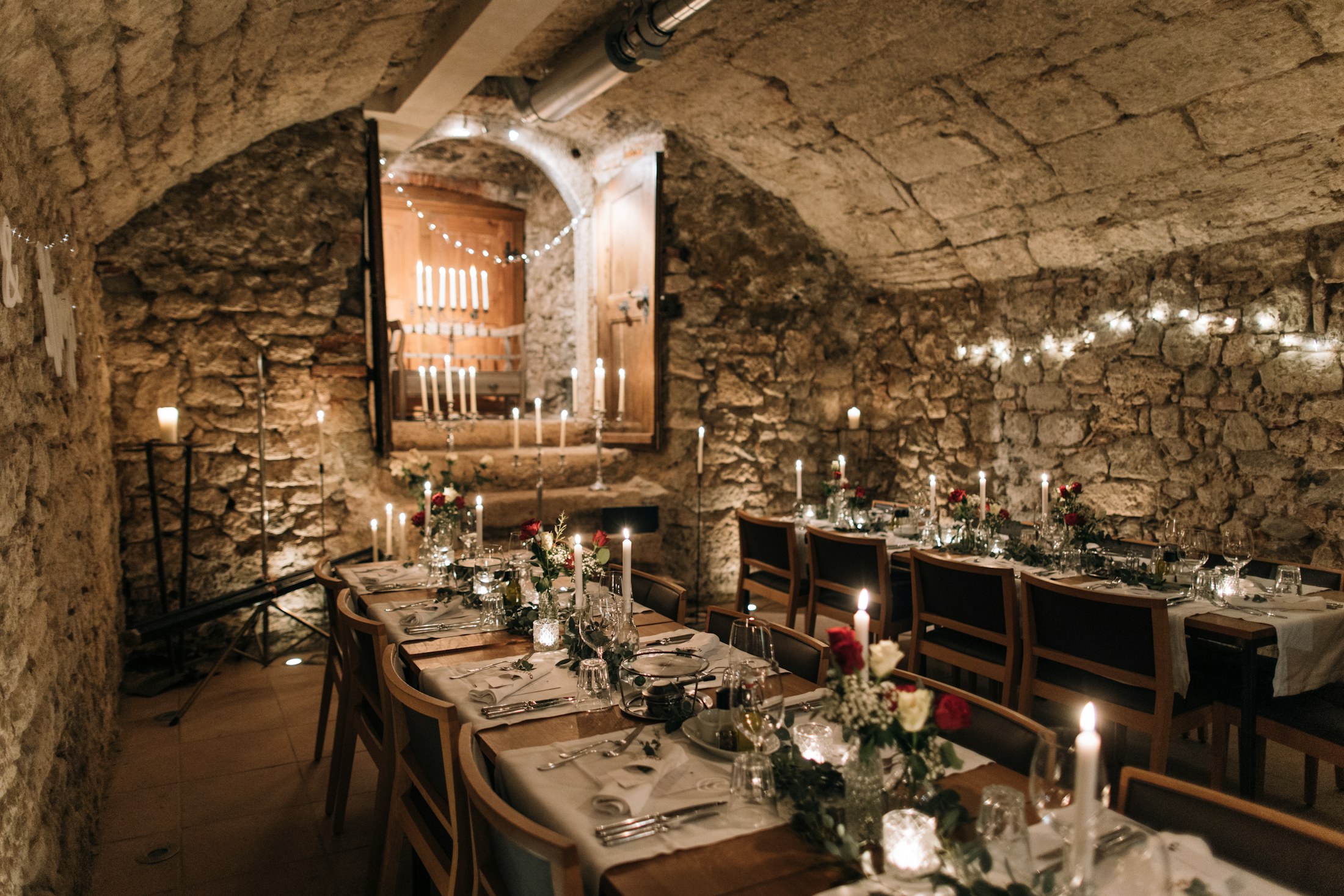 Long candlelit dinner tables inside an old stone cellar
