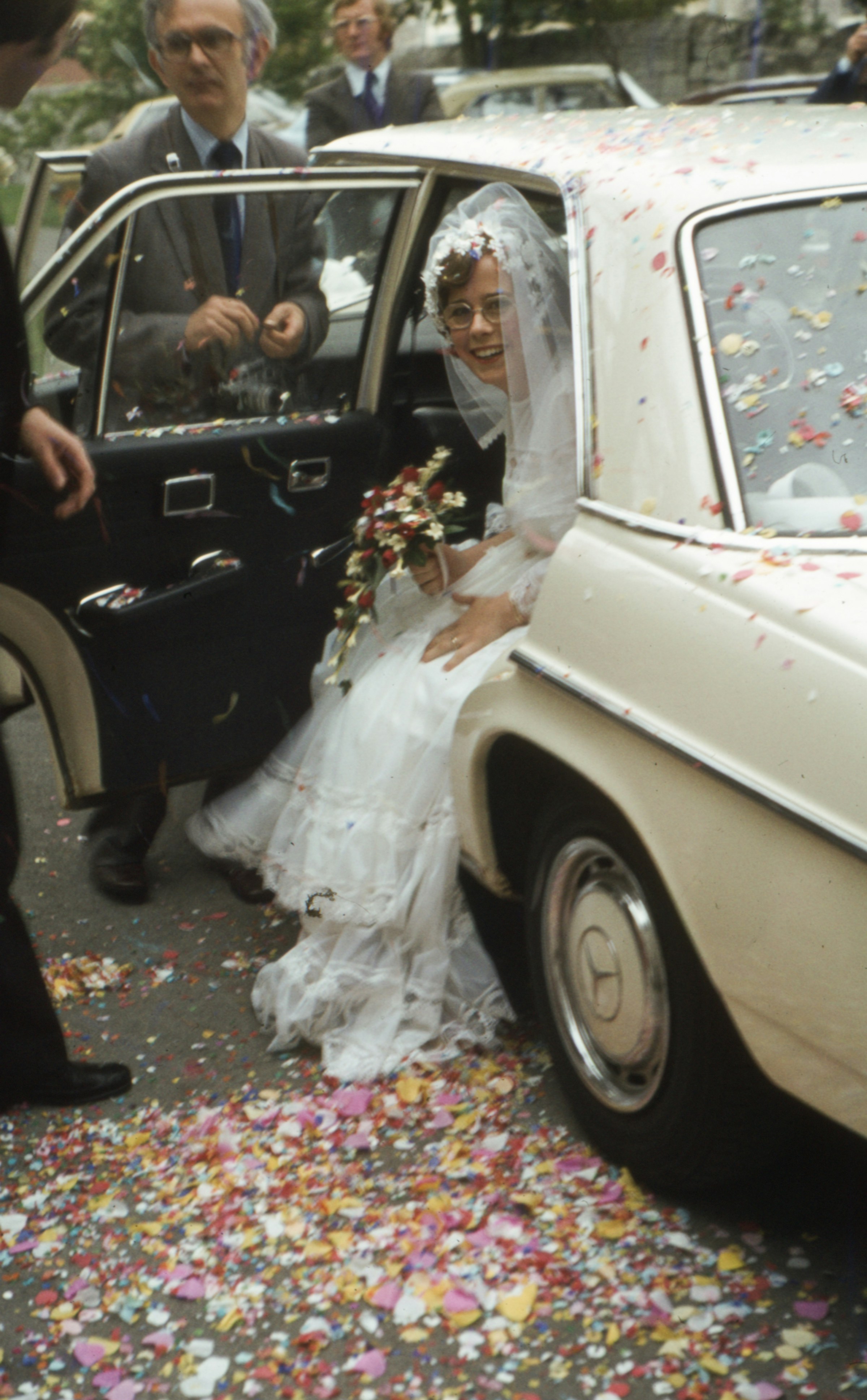 A bride stepping from a vintage car through confetti, photographed on film